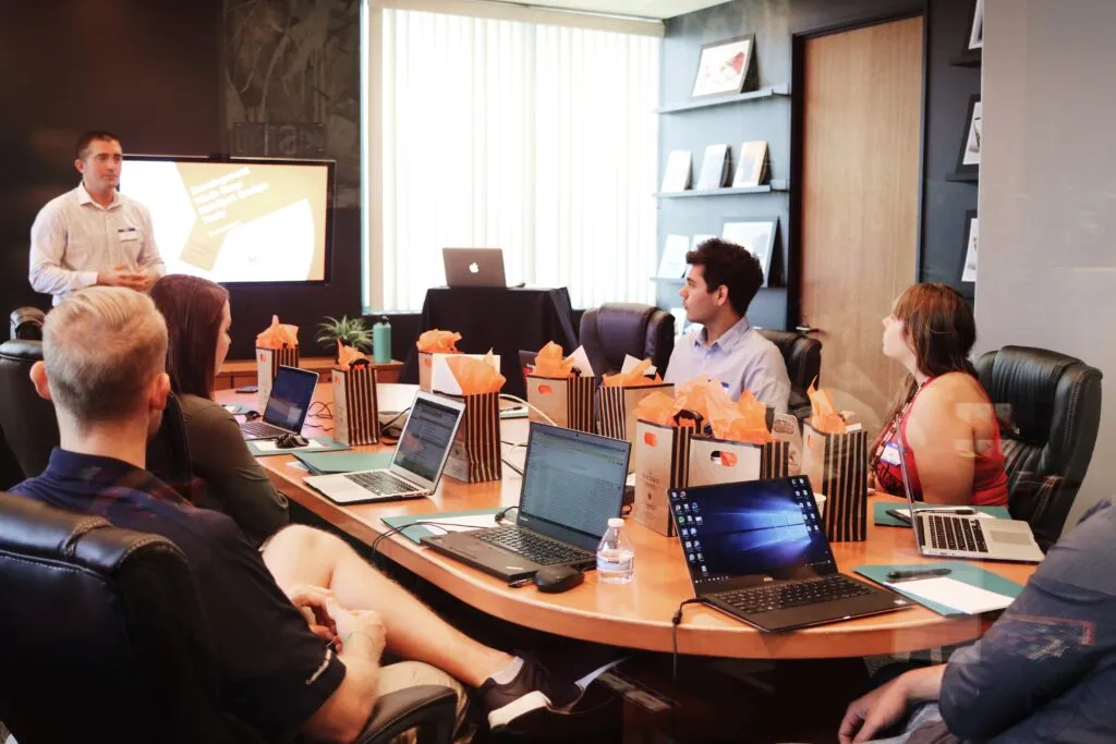 Group of white people around a table attending a meeting with computers